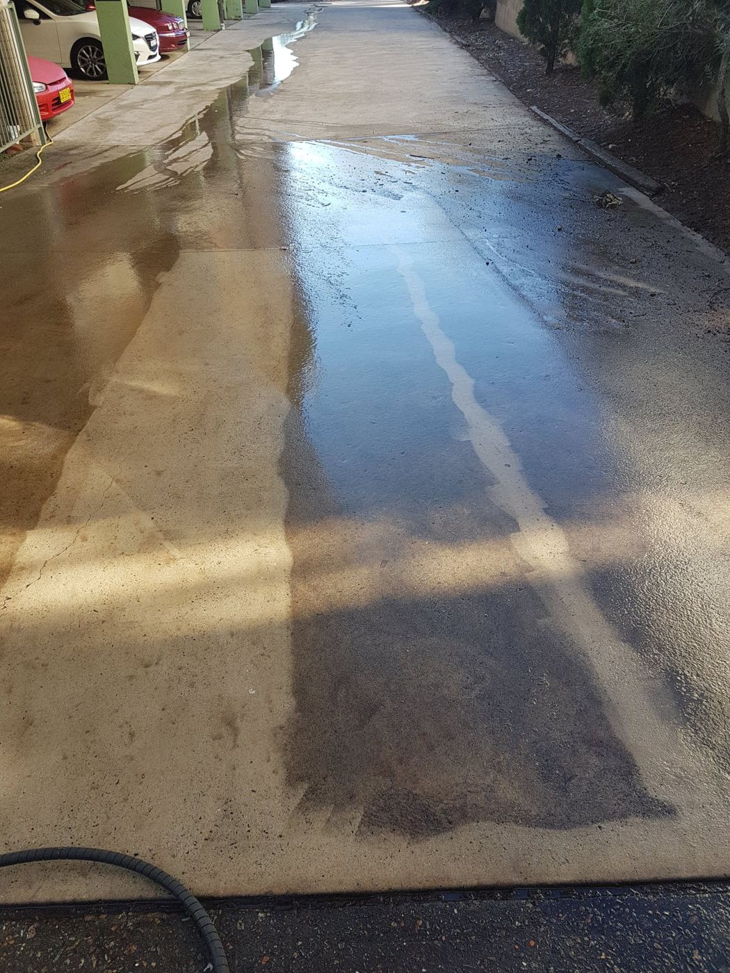 Concrete driveway mid pressure wash, with a clean strip beside dirty concrete